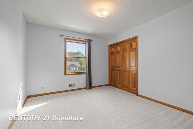 unfurnished bedroom featuring light carpet, a closet, and a textured ceiling