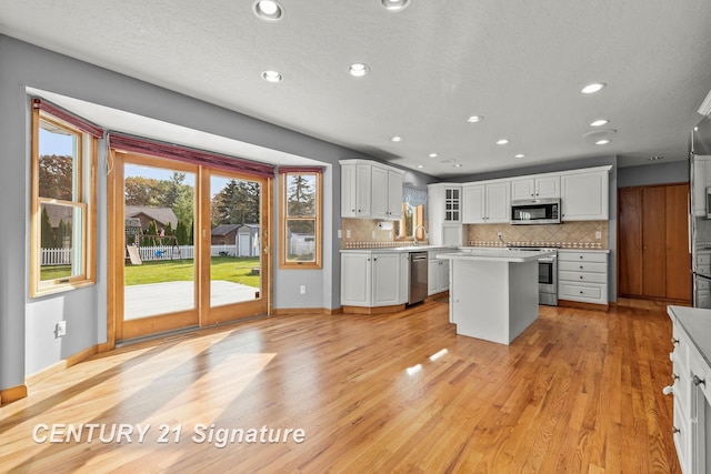 kitchen with decorative backsplash, appliances with stainless steel finishes, white cabinets, light hardwood / wood-style floors, and a kitchen island