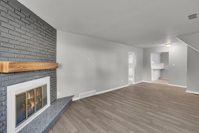 unfurnished living room featuring hardwood / wood-style flooring and a brick fireplace