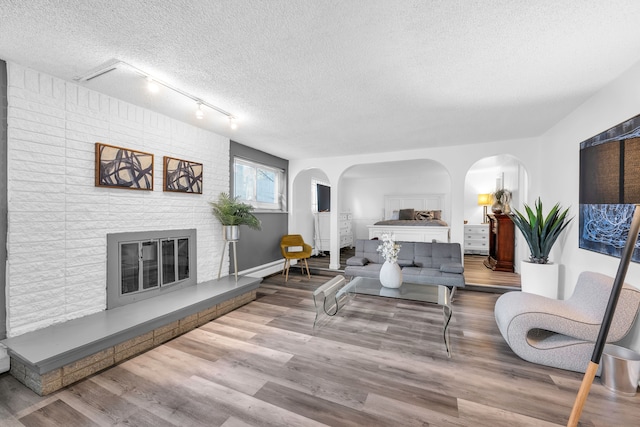 living room featuring hardwood / wood-style flooring, track lighting, a textured ceiling, and a brick fireplace