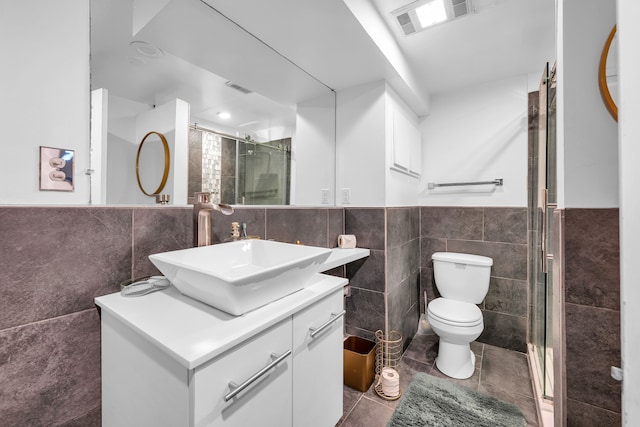 bathroom featuring vanity, a shower with door, tile patterned floors, toilet, and tile walls