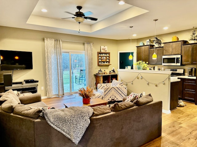 living room with light hardwood / wood-style floors, ceiling fan, and a tray ceiling