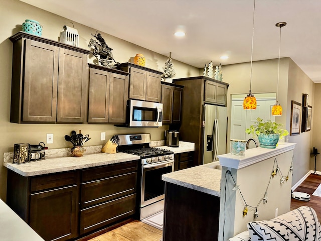 kitchen featuring dark brown cabinets, hanging light fixtures, appliances with stainless steel finishes, and light hardwood / wood-style flooring