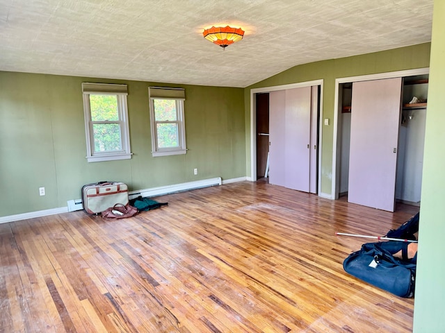 unfurnished bedroom featuring baseboard heating, multiple closets, wood-type flooring, and lofted ceiling