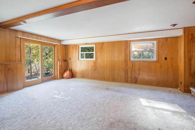 carpeted spare room with beam ceiling, plenty of natural light, and wooden walls