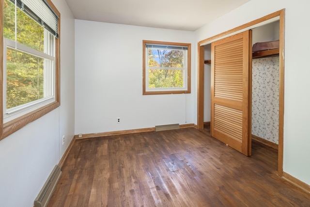 unfurnished bedroom featuring a closet, dark wood-type flooring, and a baseboard heating unit