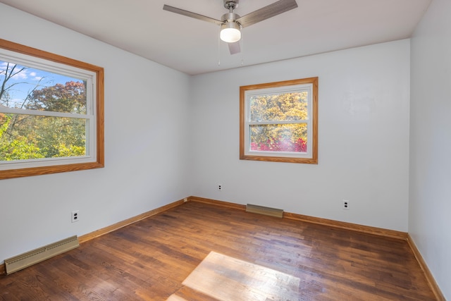 unfurnished room featuring a wealth of natural light, dark hardwood / wood-style flooring, baseboard heating, and ceiling fan