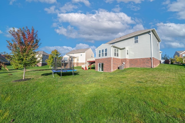 rear view of house with a trampoline, a yard, and central air condition unit