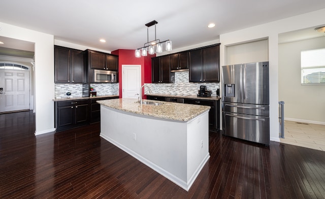 kitchen with appliances with stainless steel finishes, a kitchen island with sink, sink, pendant lighting, and dark hardwood / wood-style floors