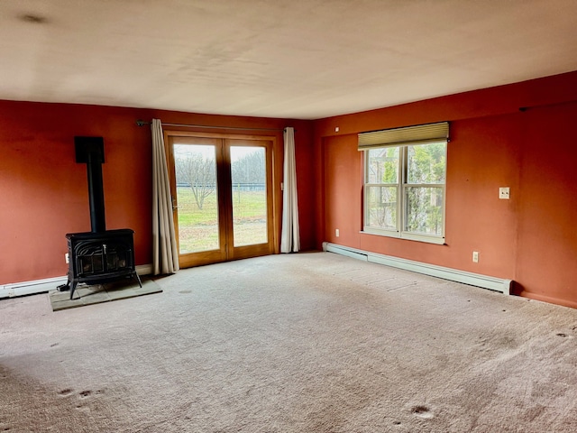 unfurnished living room featuring carpet flooring, a wood stove, and a baseboard radiator