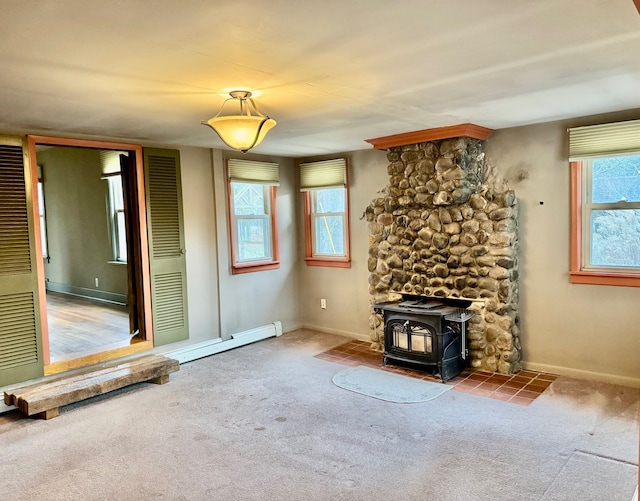 unfurnished living room featuring carpet flooring, a wood stove, baseboard heating, and a wealth of natural light