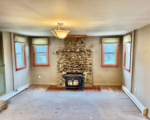 unfurnished living room featuring carpet flooring, a baseboard heating unit, a wood stove, and a healthy amount of sunlight