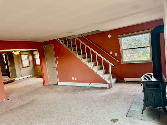 unfurnished living room featuring carpet, baseboard heating, a wood stove, and a wealth of natural light