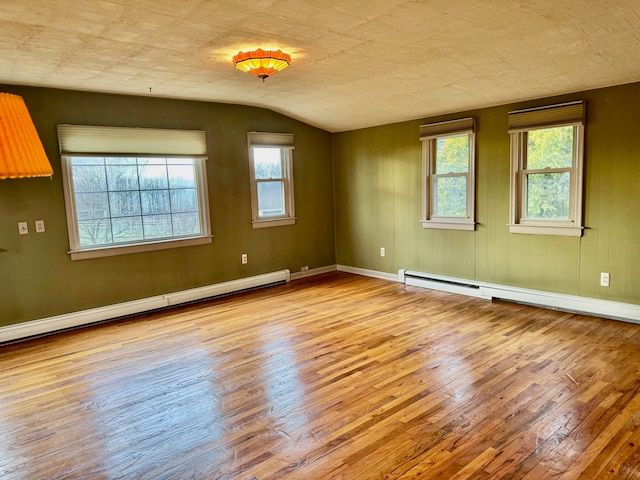 empty room featuring light hardwood / wood-style flooring, lofted ceiling, and a baseboard heating unit