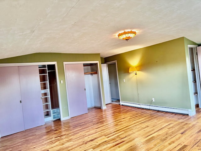 unfurnished bedroom featuring two closets, light hardwood / wood-style floors, vaulted ceiling, and a baseboard radiator