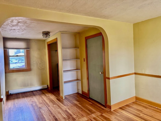 unfurnished bedroom featuring a textured ceiling, hardwood / wood-style flooring, and baseboard heating