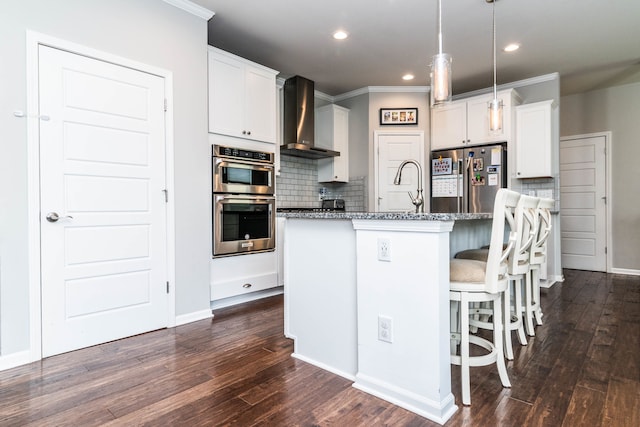 kitchen with wall chimney range hood, dark stone countertops, a center island with sink, white cabinetry, and stainless steel appliances