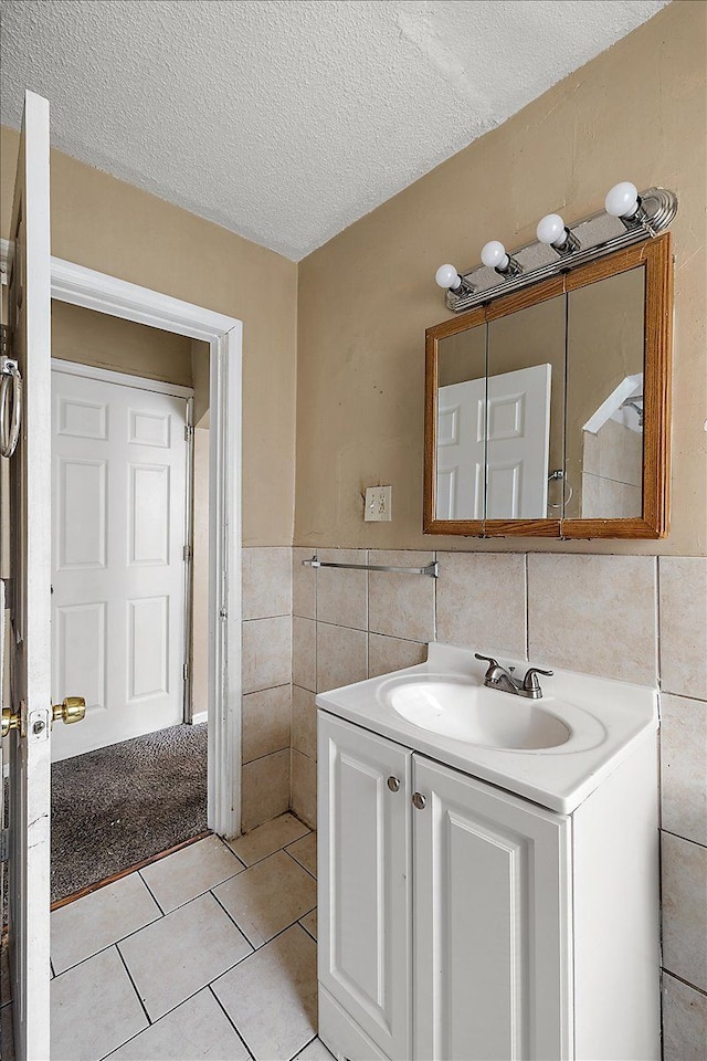 bathroom with a textured ceiling, tile patterned flooring, tile walls, and vanity