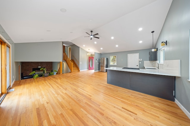 unfurnished living room with lofted ceiling, sink, ceiling fan, a fireplace, and light hardwood / wood-style floors