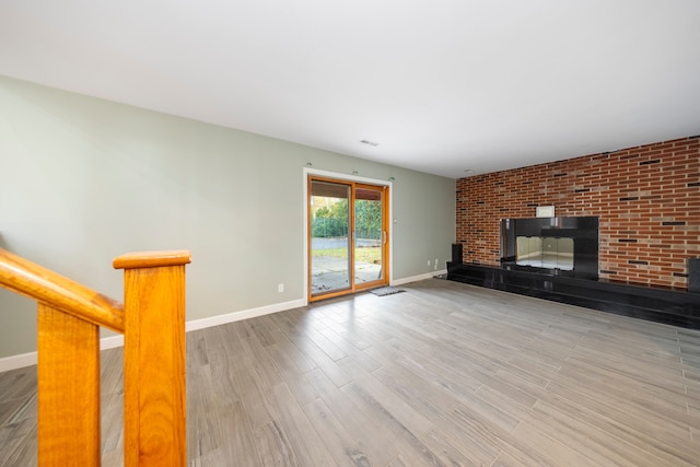 unfurnished living room with a fireplace, wood-type flooring, and brick wall