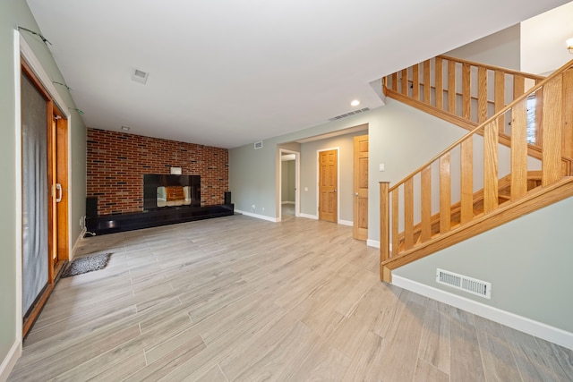 unfurnished living room with a brick fireplace, brick wall, and light wood-type flooring