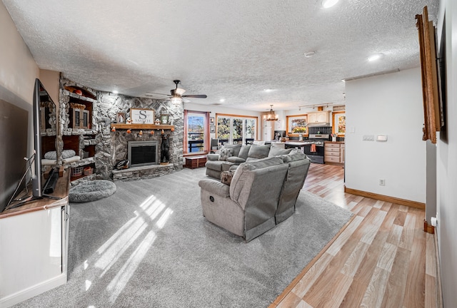 living room featuring a fireplace, ceiling fan, a textured ceiling, and light hardwood / wood-style flooring