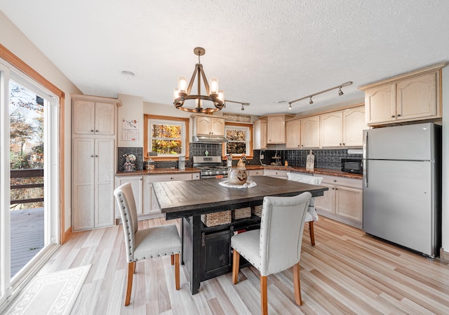 kitchen with light brown cabinets, hanging light fixtures, light hardwood / wood-style floors, stainless steel appliances, and a chandelier