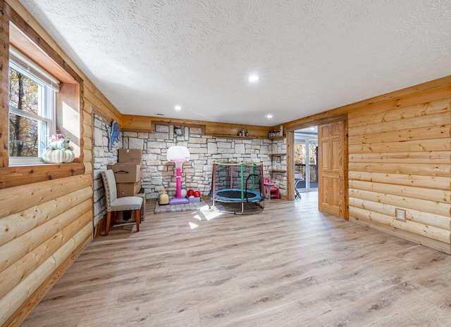 unfurnished room with rustic walls, a textured ceiling, and light wood-type flooring