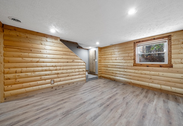 unfurnished room with a textured ceiling, log walls, and light hardwood / wood-style flooring