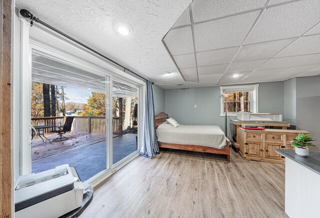 bedroom with a drop ceiling, access to exterior, and light wood-type flooring