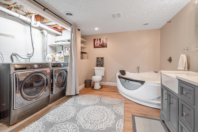 laundry room with sink, washing machine and dryer, a textured ceiling, and light hardwood / wood-style flooring