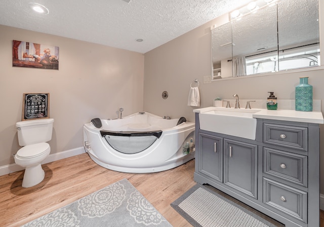 bathroom featuring a textured ceiling, vanity, hardwood / wood-style flooring, toilet, and a tub