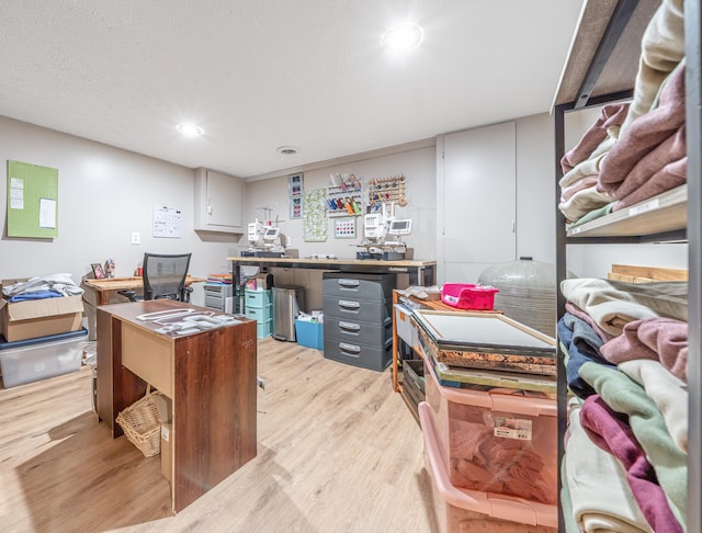 home office with a textured ceiling, a workshop area, and light hardwood / wood-style flooring