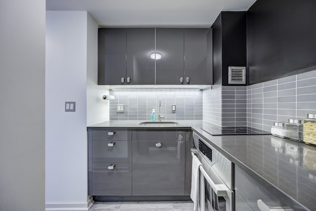 kitchen featuring gray cabinetry, oven, sink, and tasteful backsplash