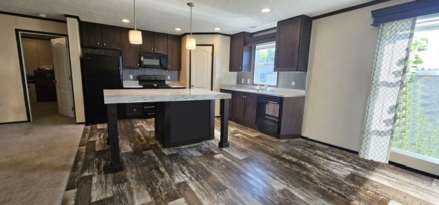 kitchen featuring dark brown cabinetry, a breakfast bar area, decorative backsplash, a kitchen island, and black appliances