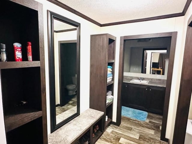 interior space with hardwood / wood-style floors, vanity, toilet, ornamental molding, and a textured ceiling