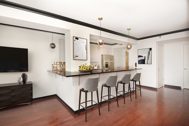 kitchen with kitchen peninsula, stainless steel fridge, a kitchen breakfast bar, decorative light fixtures, and white cabinetry