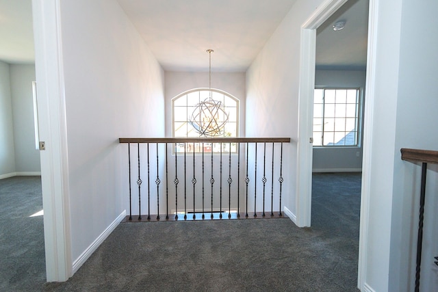 hallway with a chandelier and dark colored carpet