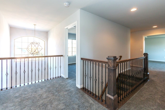 hallway featuring dark colored carpet, an inviting chandelier, and plenty of natural light