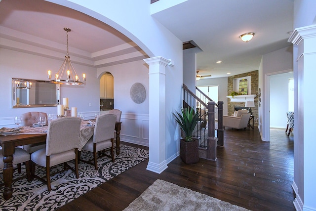 dining area with a fireplace, dark hardwood / wood-style flooring, decorative columns, and ceiling fan with notable chandelier