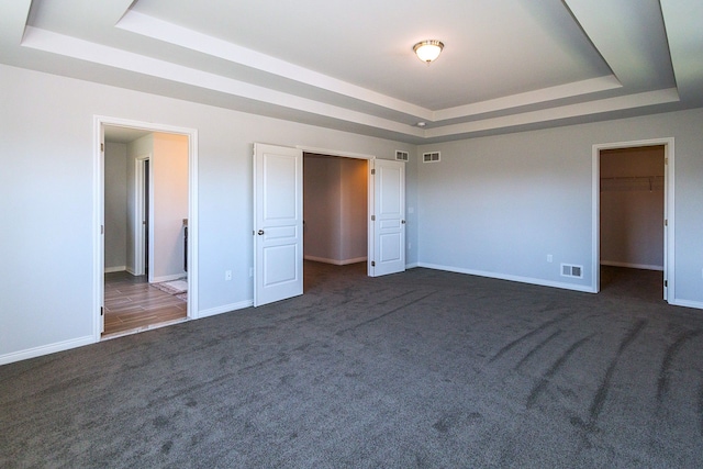 unfurnished bedroom featuring a walk in closet, a tray ceiling, dark carpet, and a closet