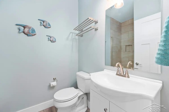 bathroom with a tile shower, hardwood / wood-style flooring, vanity, and toilet