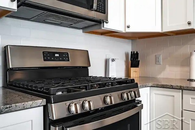 kitchen featuring white cabinets, backsplash, stainless steel appliances, and dark stone counters