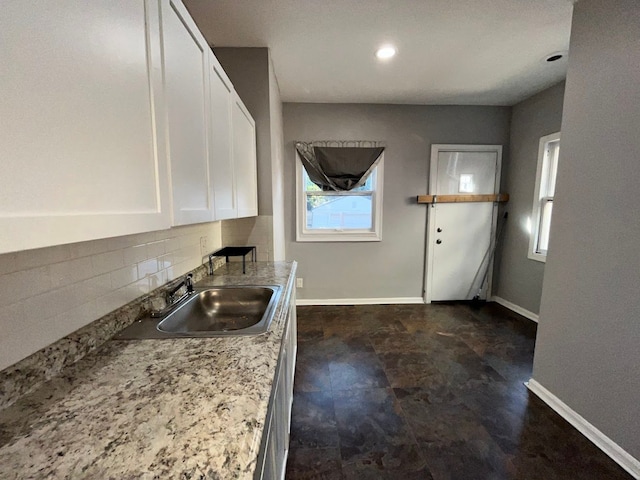 kitchen with decorative backsplash, white cabinetry, sink, and light stone countertops