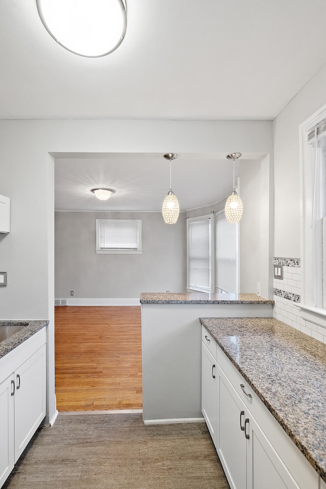 kitchen featuring hardwood / wood-style flooring, light stone countertops, a wealth of natural light, decorative light fixtures, and white cabinetry