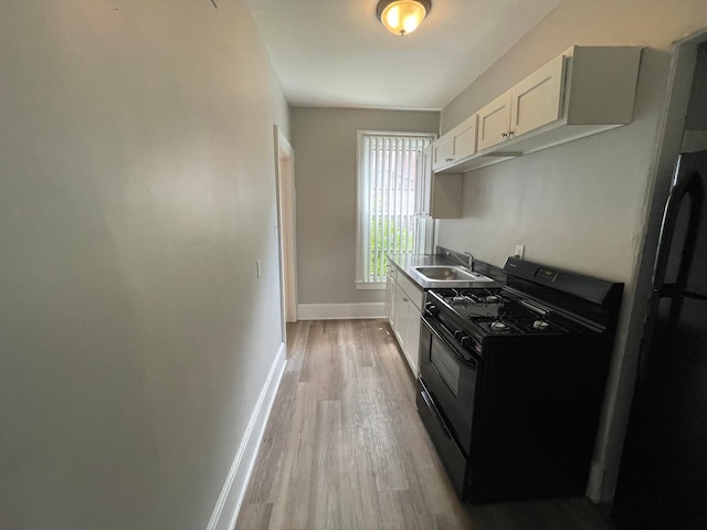 kitchen featuring black gas range, light wood-type flooring, white cabinetry, and sink