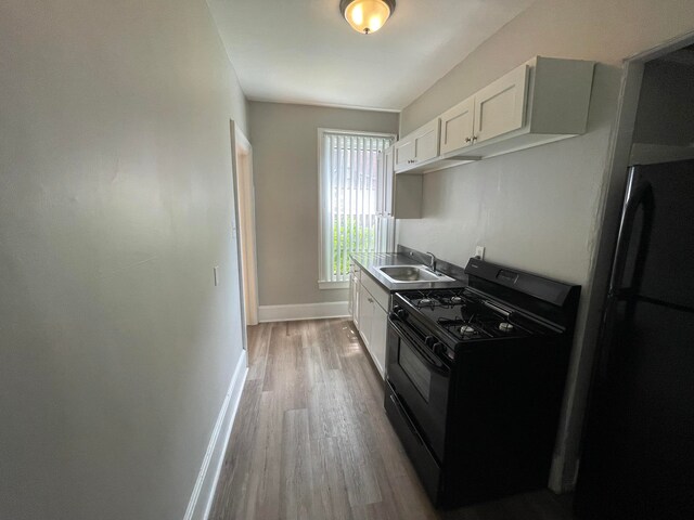 kitchen with sink, refrigerator, black range with gas cooktop, light hardwood / wood-style floors, and white cabinets