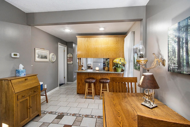 kitchen featuring white refrigerator, kitchen peninsula, a breakfast bar area, and light tile patterned floors