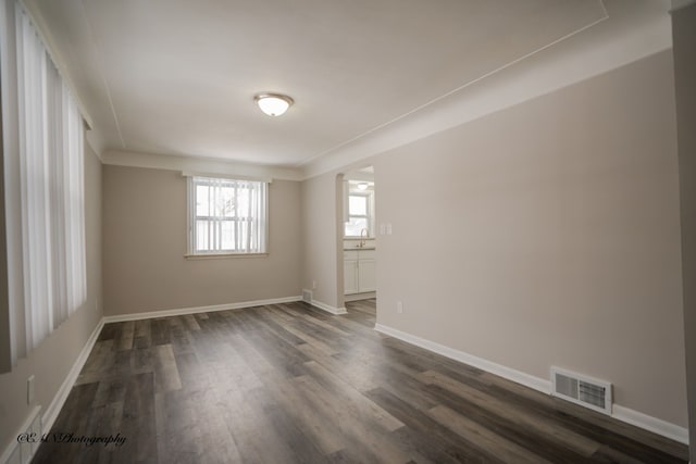 empty room with baseboards, visible vents, dark wood-type flooring, and a sink