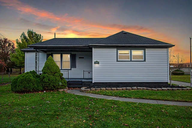 view of front of property with a shingled roof, a porch, fence, and a front lawn